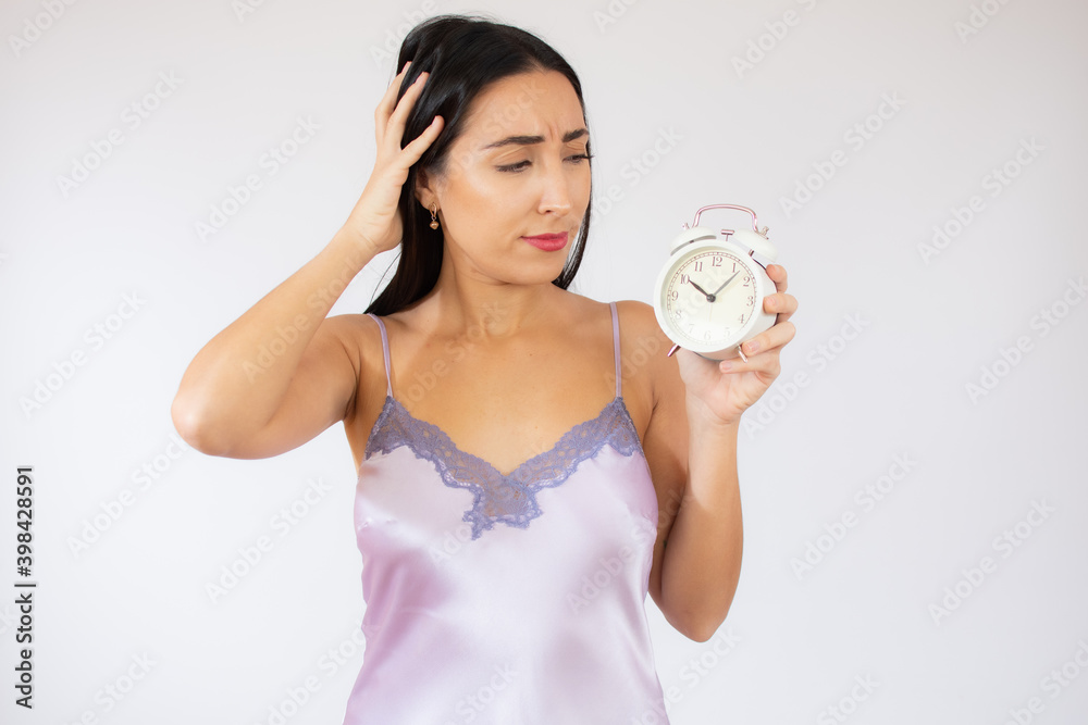 Beautiful young woman in dressing gown holding alarm clock over white background. Beautiful young woman in dressing gown holding alarm clock over white background.