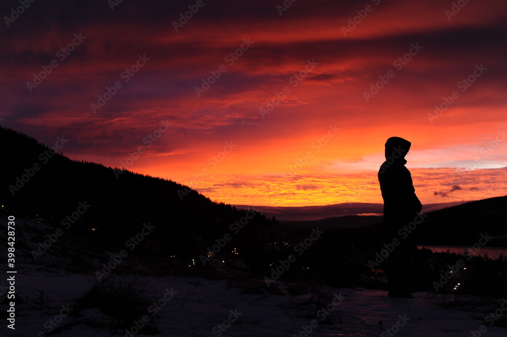 Black silhouette on mountain plateau during sunset with colorful red, violet, orange sky and clouds in winter in Scandinavia