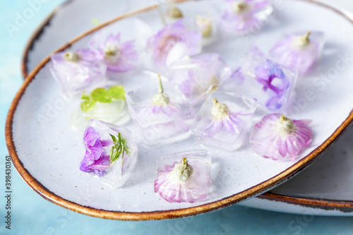 Plates with frozen flowers in ice on color background