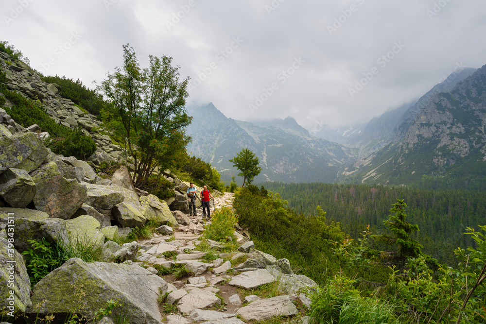 Two hikers standing on rock trail in mountains. High peaks of mountains in the fog.