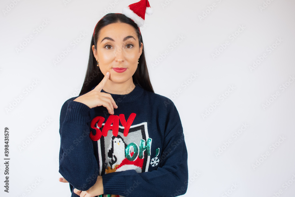 Fototapeta premium Young beautiful woman wearing santa hat over white isolated background confuse and wondering about question. Uncertain with doubt, thinking with hand on face. Pensive concept.