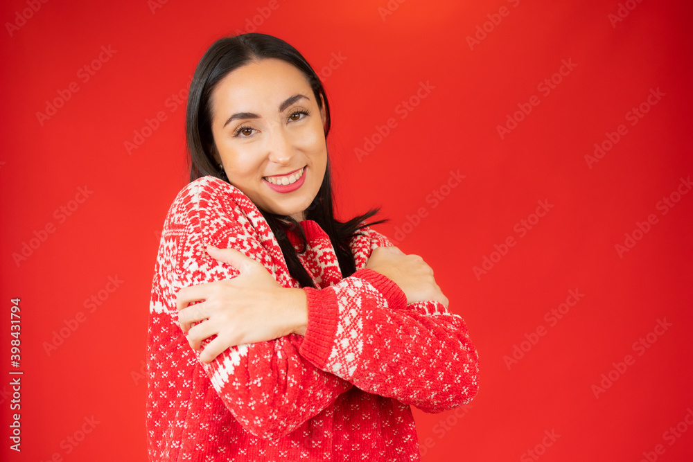 Portrait of a pretty young woman in red sweater hugging herself. Concept of selfish emotion.
