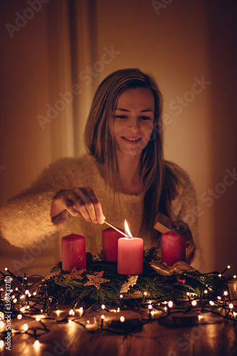 young woman with highlighted hair lights the first candle from an Advent wreath. Young beautiful woman smiling on her lip with Christmas approaching. Traditions of the family and European countries photo