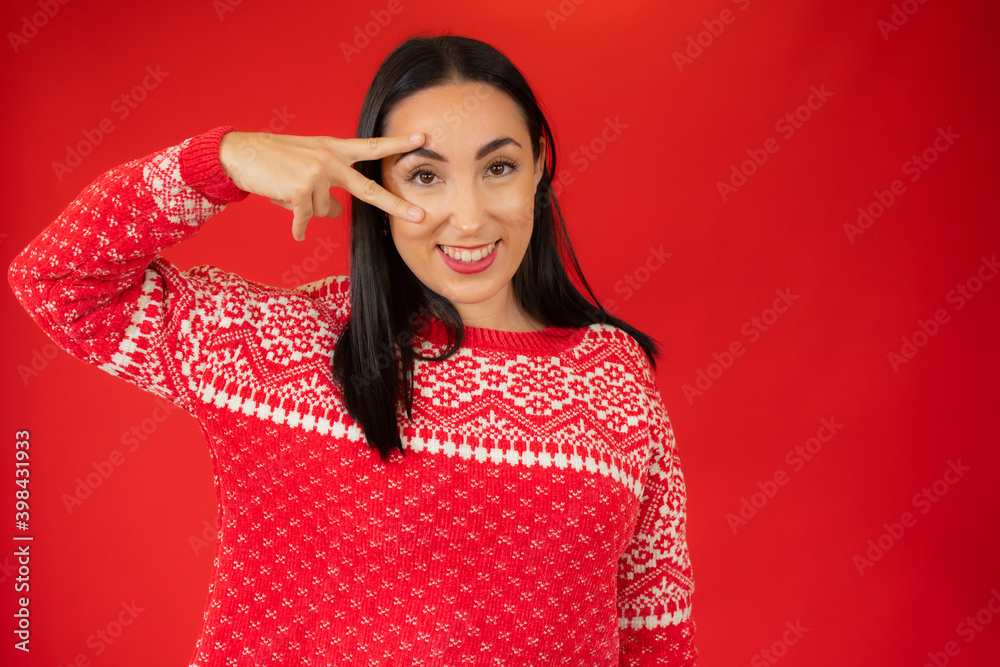 Portrait of gorgeous brunette woman looking at camera with smile and showing peace sign with fingers isolated over red background Portrait of gorgeous brunette woman looking at camera with smile and showing peace sign with fingers isolated over red background