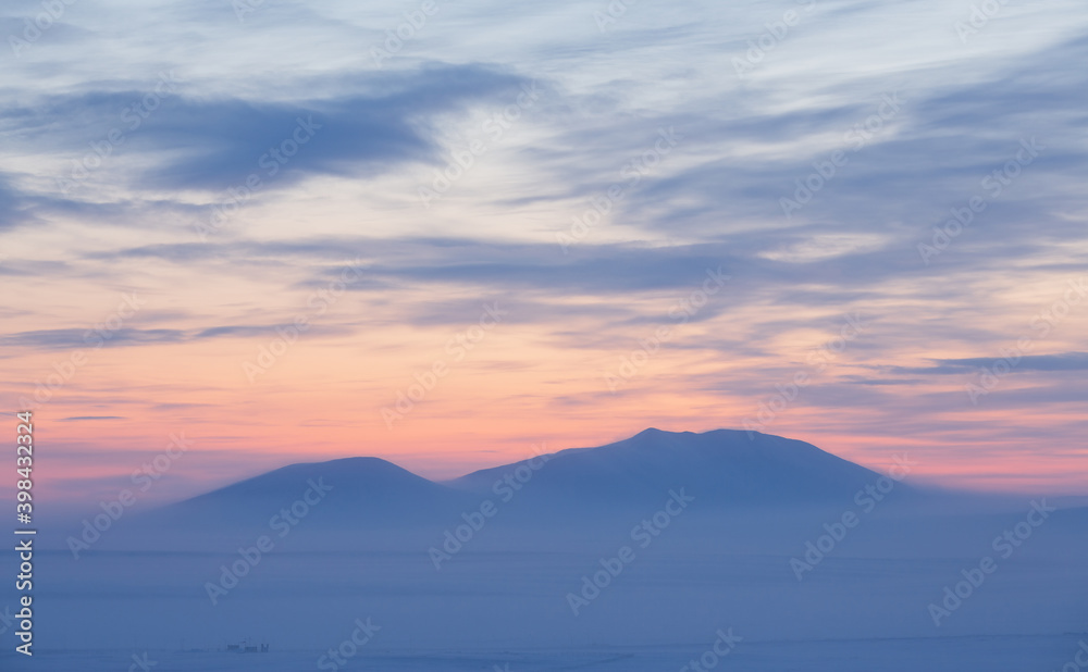 Winter arctic landscape. Cold winter weather. Frosty fog over the tundra. View of the snow-capped mountains at sunset. Picturesque arctic nature. Mount Dionysius, Chukotka, Siberia, Far East Russia.