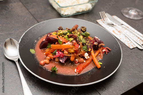 Mixed raw vegetables with raisins and pistachio on black plate on dark dining table