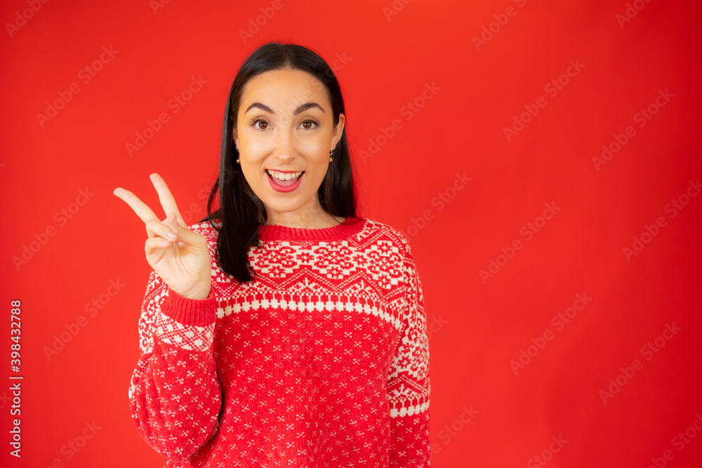 Portrait of gorgeous brunette woman looking at camera with smile and showing peace sign with fingers isolated over red background Portrait of gorgeous brunette woman looking at camera with smile and showing peace sign with fingers isolated over red background