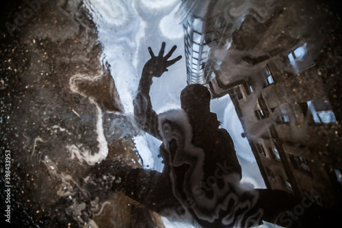 Silhouette of man reflected in puddle with oil slick