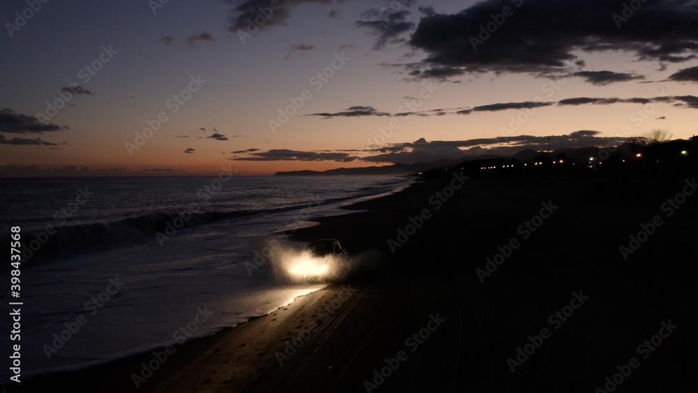 Macchina di notte che cammina sulla spiaggia con i fari accesi. Vista aerea
