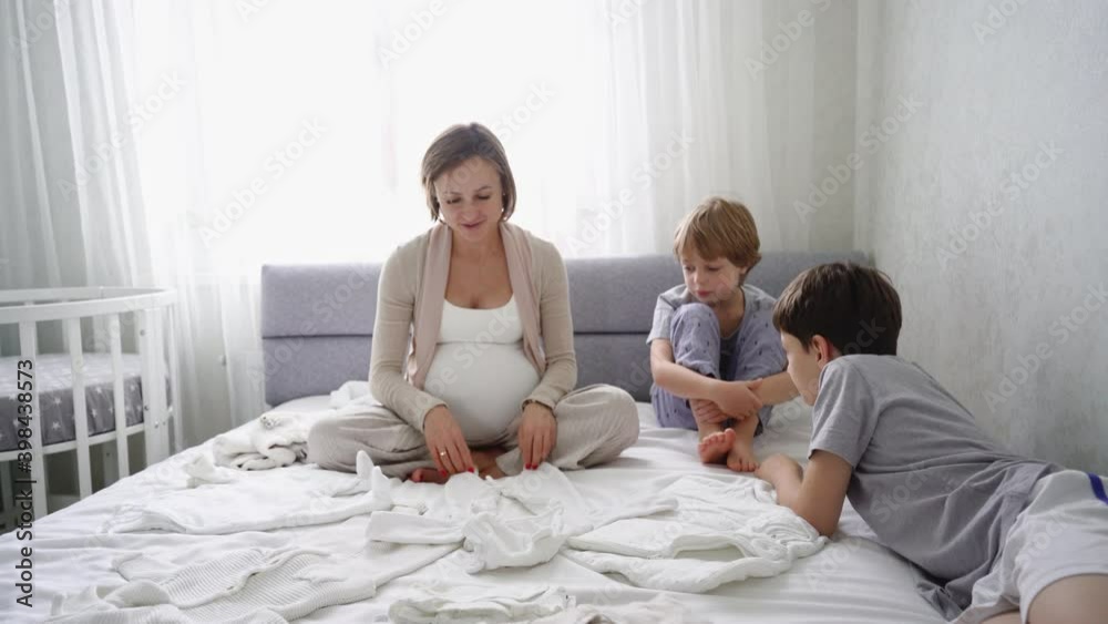 Pregnant woman sits on the bed with two sons and prepares things for the birth of a child. High quality 4k footage Pregnant woman sits on the bed with two sons and prepares things for the birth of a child. High quality 4k footage