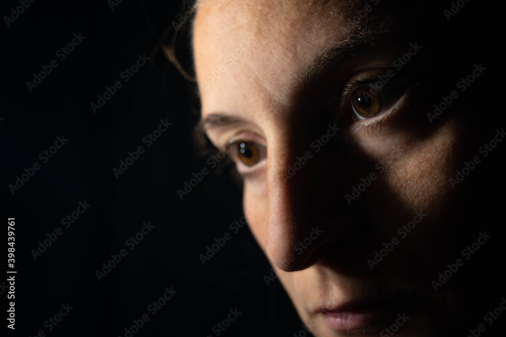Close-up of a dark portrait of a very dimly lit woman. The woman is looking at infinity, transmitting a feeling of sadness or depresion Close-up of a dark portrait of a very dimly lit woman. The woman is looking at infinity, transmitting a feeling of sadness or depresion