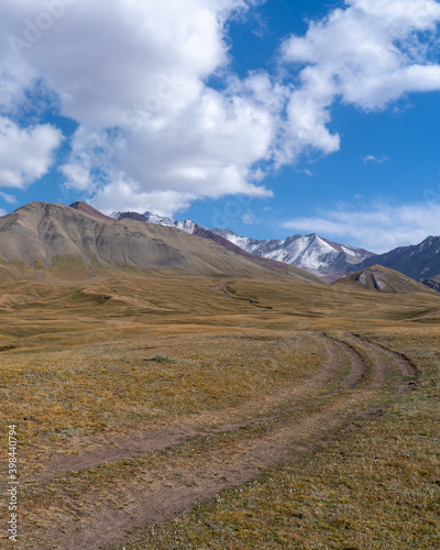 Dirt track in summer pasture in Sary Tash valley, Kyrgyzstan with snow-capped Trans-Alay mountain range background along the high-altitude Pamir Highway near Tajikistan border