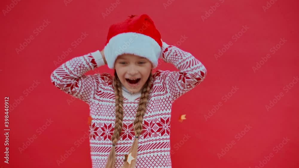 happy girl in santa hat and christmas sweater under confetti isolated on red happy girl in santa hat and christmas sweater under confetti isolated on red