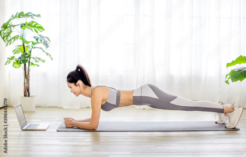 Young woman in sportswear watching online video with fitness exercises on laptop Young woman in sportswear watching online video with fitness exercises on laptop
