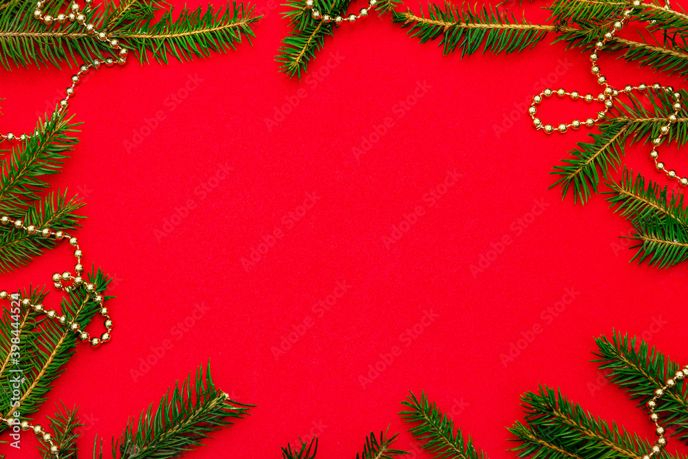 Christmas background with fresh Xmas tree branches and New Year gold beads on red background