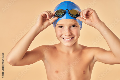 Joyful boy swimmer standing against light orange background