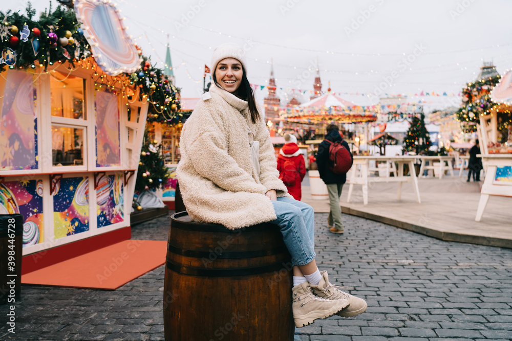 Cheerful woman sitting on barrel near illuminated cafe