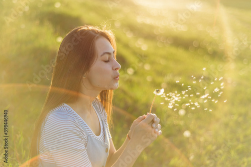 a young girl blows away a dandelion in summer. portrait of a woman in the sun