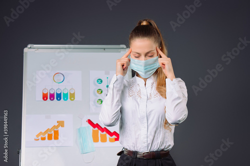 A girl, a businesswoman in a medical mask holds her hands at her temples during office conference. Diagrams. photo