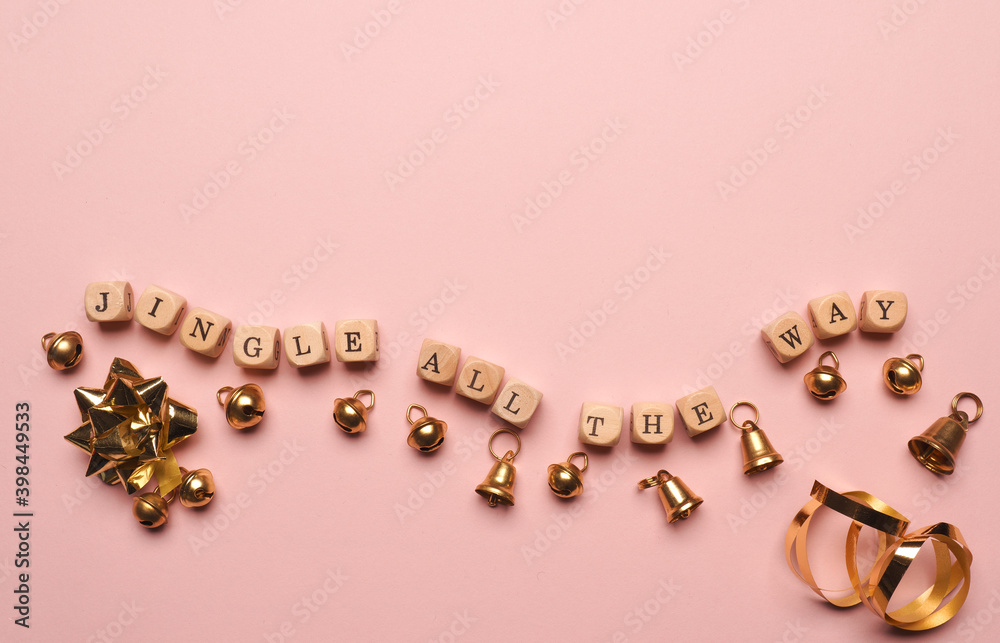 Small wooden block s with the inscription Jingle all the way and golden bells on a pink background, space for text Small wooden block s with the inscription Jingle all the way and golden bells on a pink background, space for text