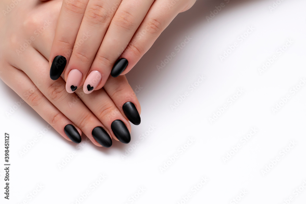 Black, beige matte manicure on long oval nails with painted black hearts on a white background close-up
