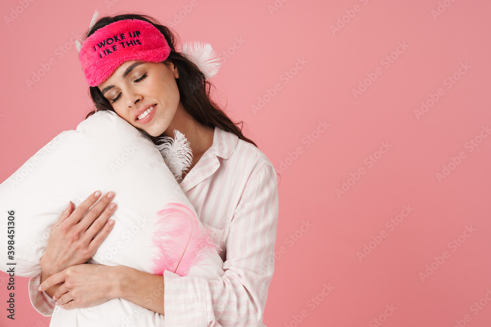 Cheerful beautiful woman in sleeping mask smiling and hugging pillow