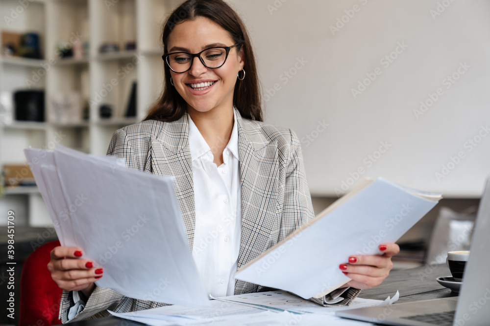 Beautiful cheerful woman in eyeglasses working with laptop and papers Beautiful cheerful woman in eyeglasses working with laptop and papers