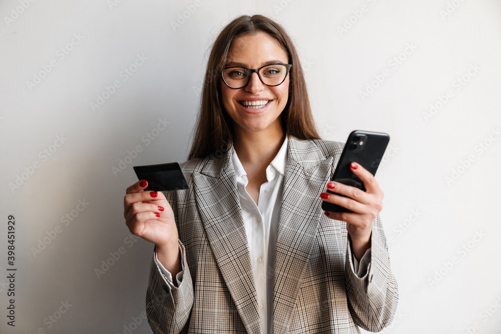 Beautiful joyful businesswoman posing with credit card and cellphone