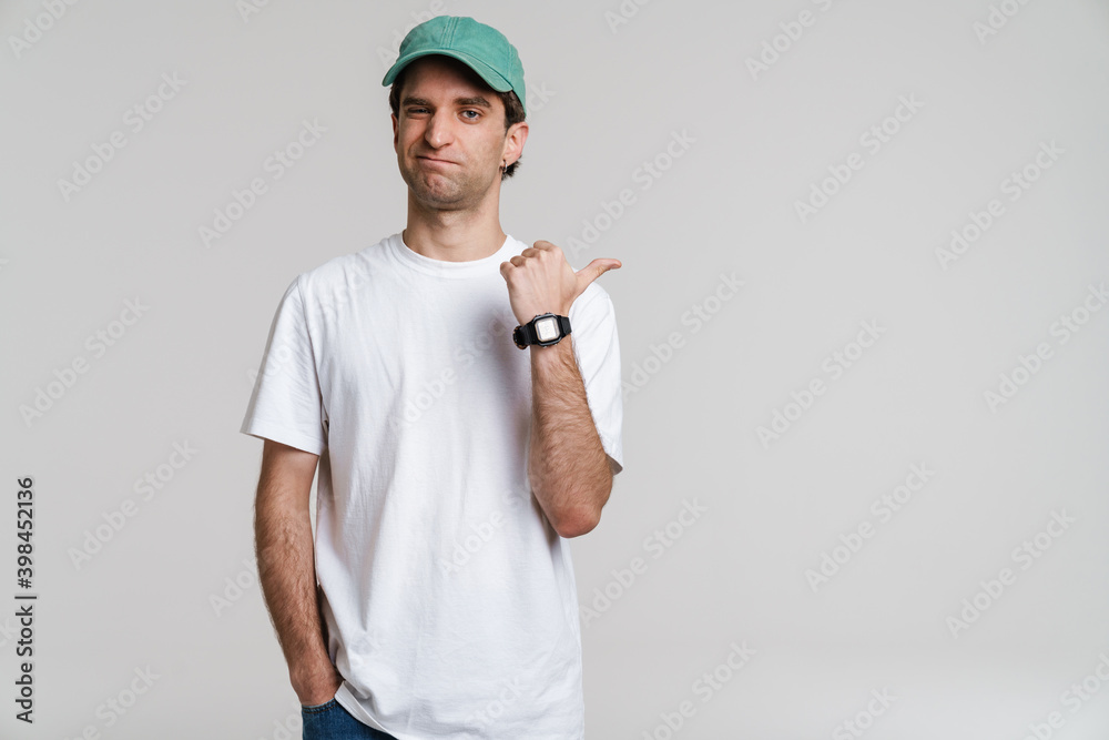 Young displeased man in cap winking and pointing finger aside Young displeased man in cap winking and pointing finger aside