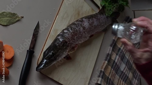 Woman sprinkles salt on pike lying on cutting board for baking in  oven.