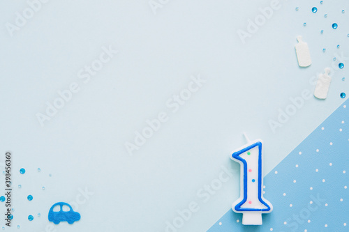 One year background. Candle in shape of number one lies on blue background with children's accessories. Boy birthday concept. Mock up for greeting card. Copy space.