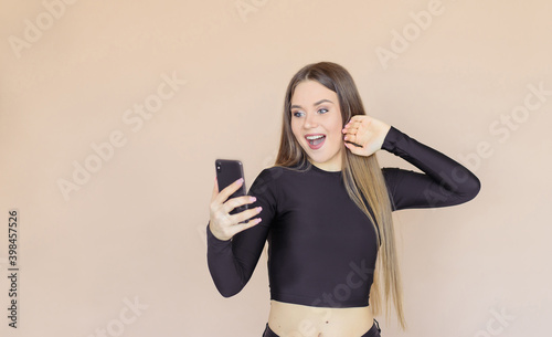 The girl looks at the phone with surprise, delight and joy. Beige background.
