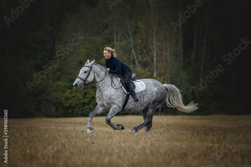 Smiling woman riding a galloping horse on the meadow.