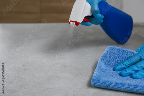 Woman in gloves cleaning light grey stone table with rag and detergent indoors, closeup. Space for text