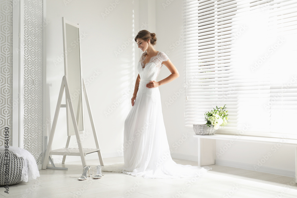 Young bride in beautiful wedding dress near mirror indoors Young bride in beautiful wedding dress near mirror indoors