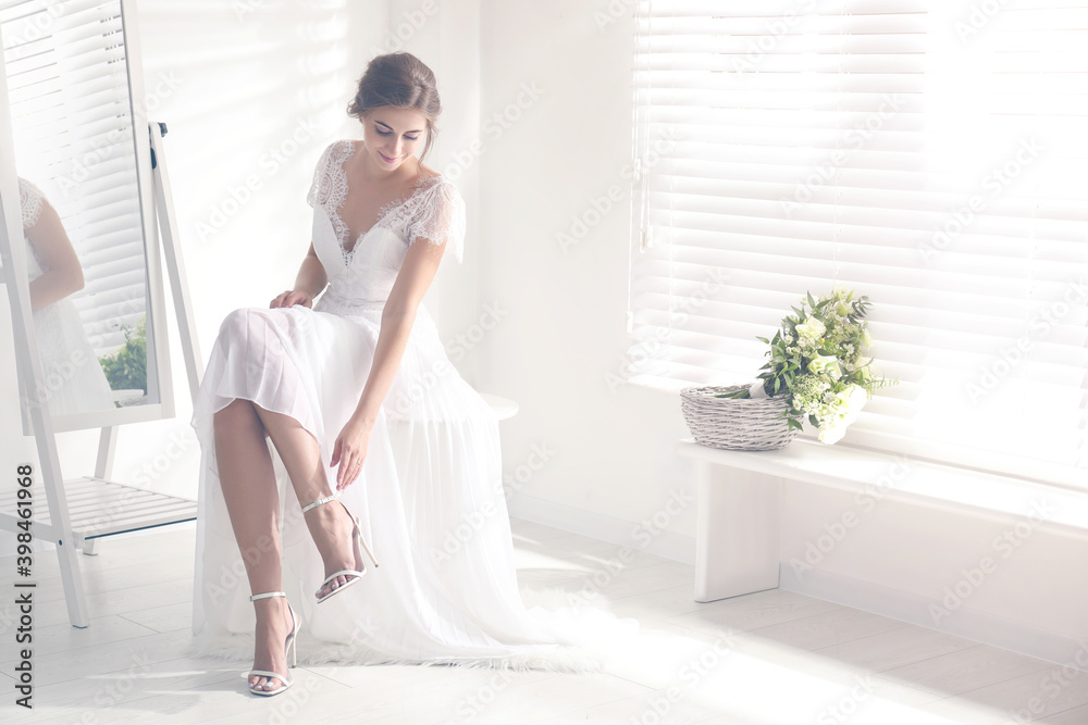 Young bride in beautiful wedding dress putting on shoes near mirror indoors Young bride in beautiful wedding dress putting on shoes near mirror indoors
