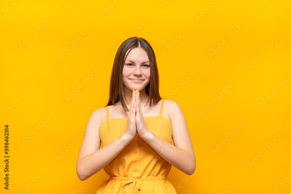 Young beautiful caucasian woman in a yellow sweater on a yellow background prays with her hands together, asking for forgiveness, smiling confidently. Young beautiful caucasian woman in a yellow sweater on a yellow background prays with her hands together, asking for forgiveness, smiling confidently.