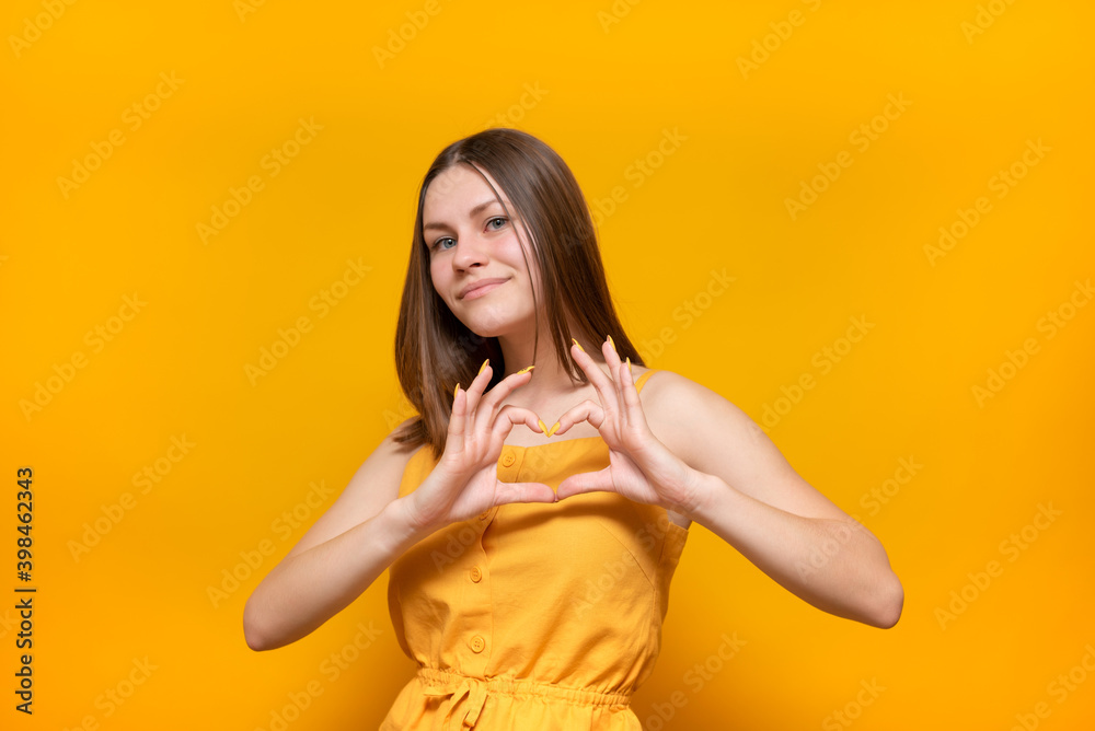 Young beautiful caucasian woman in a yellow sweater on a yellow background smiling in love, making a heart symbol shape with her hands. Romantic concept. Young beautiful caucasian woman in a yellow sweater on a yellow background smiling in love, making a heart symbol shape with her hands. Romantic concept.