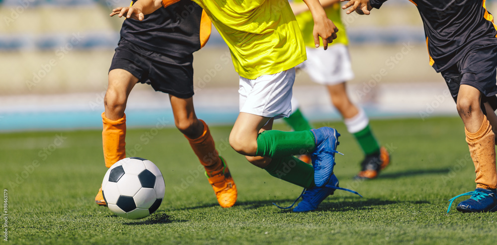 Children soccer players in a football duel running after ball on a game. Sports stadium in the background Children soccer players in a football duel running after ball on a game. Sports stadium in the background