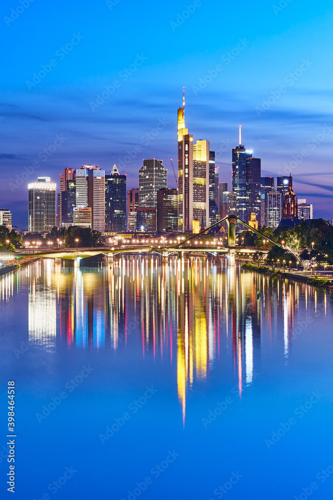 Fototapeta premium Nicely illuminated skyline of Frankfurt, Germany, in the evening with reflections on the river Main
