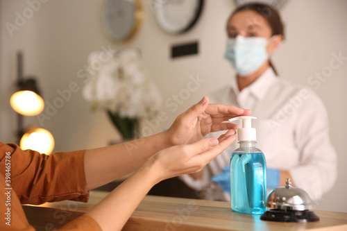 Woman applying antiseptic gel at hotel reception, closeup photo