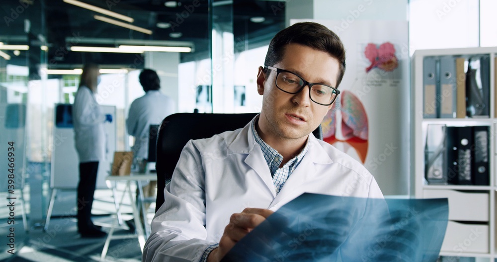 Fototapeta premium Online doctor consulting. Male doctor talking directly to the camera on online call with patient via web cam, explaining and discussing X-ray scan. Telemedicine concept. Medical consultation. Close up