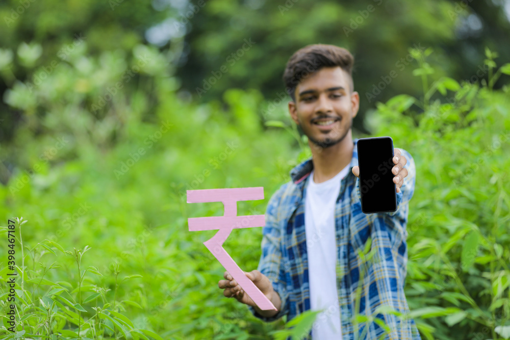 Young indian man holding indian rupees symbol in hand over nature background Young indian man holding indian rupees symbol in hand over nature background