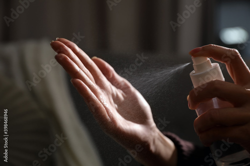 Woman spraying antiseptic onto hand against blurred background  closeup