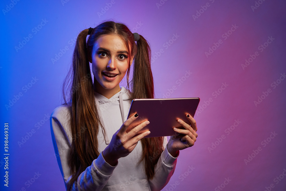 Shocked girl with digital tablet pc, neon studio background. Surprised young woman with pad, looking at camera. Shocked girl with digital tablet pc, neon studio background. Surprised young woman with pad, looking at camera.