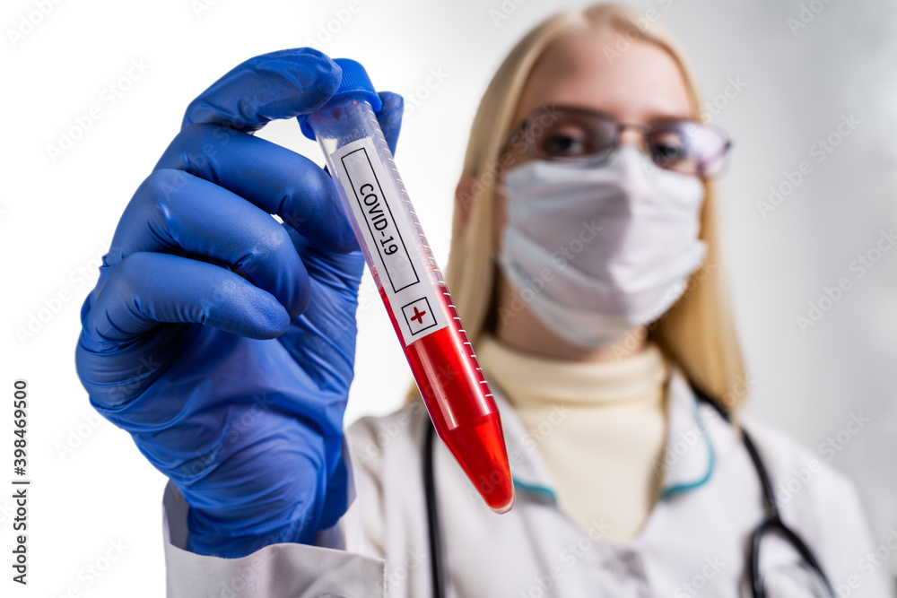 Coronavirus covid 19 infected blood vial in hand of female doctor with surgical mask and glows.