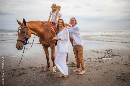 Horse riding on the beach. Two sisters on a horse. Mother leading horse by its rein. Father standing near by. Family concept. Summer vacation. Bali, Indonesia