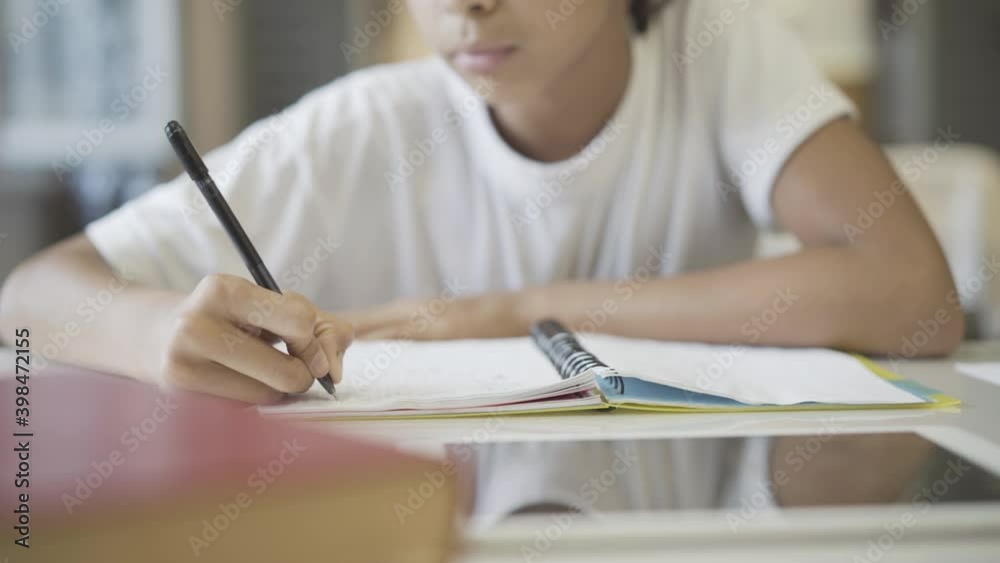 Unrecognizable African American girl writing in notebook at home. Smart student doing homework indoors. Education and lifestyle concept.