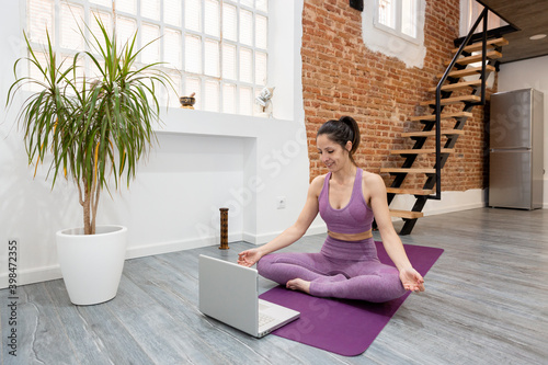 Athletic girl doing yoga meditation posture in front of her laptop at home. Concept of online classes.