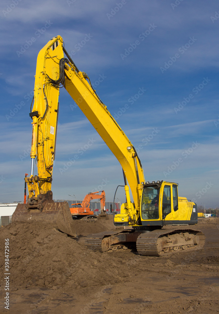 yellow used crawler excavator working on a construction site on a sunny day against a blue sky background yellow used crawler excavator working on a construction site on a sunny day against a blue sky background
